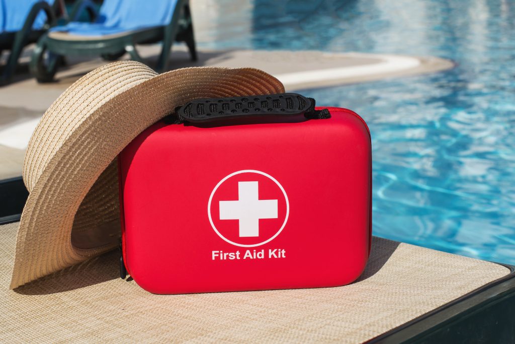 Poolside first aid kit with summer hat near resort water, vacation safety concept illustrating travel insurance, emergency preparedness, healthcare support, medicine assistance, protected leisure lifestyle